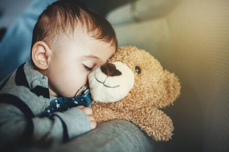 little boy sweetly sleeps on a beige teddy bear on a gray-blue backgroundの写真素材