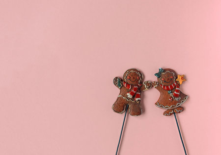 two gingerbread men a girl and a boy in Christmas clothes lie on a pink background
