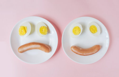 cut boiled eggs with sausage on a plate in the form of a happy and sad smiley faceの写真素材