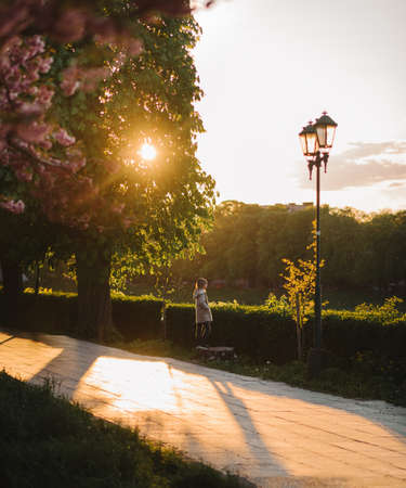 a little girl in a light coat walks along the road in a spring park in the evening at sunset background side viewの写真素材