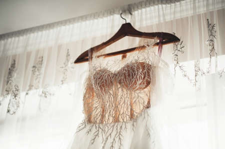 beautiful white wedding dress hanging on a hanger on the background of the window attributes wedding front view close-upの写真素材