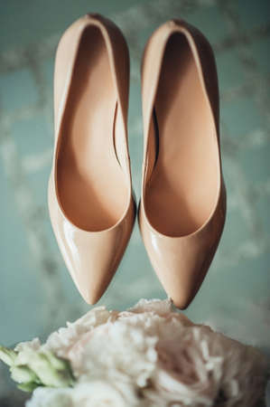 beautiful cream wedding shoes with high heels near the wedding bouquet top view, wedding attributes close-upの写真素材
