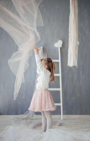 little girl playing with cloth. little girl in light clothes plays with a cloth in a light gray room side view.の写真素材