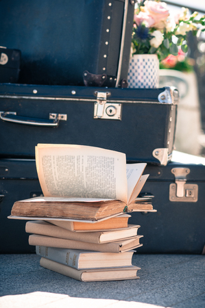 A pile of aged books on the floor with old suitcases stacked in the background, one book open by the windの写真素材
