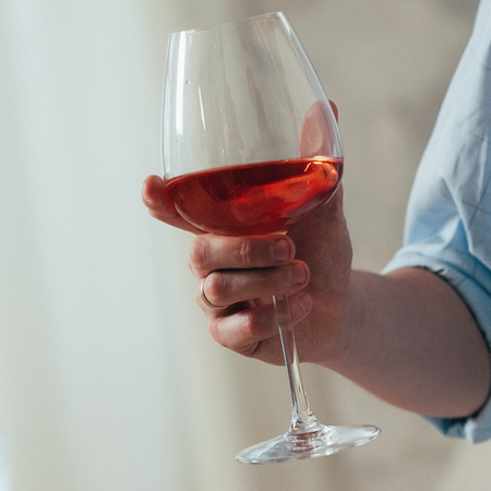 closeup of a young man in blue shirt holding a glass of red wine in his right handの写真素材
