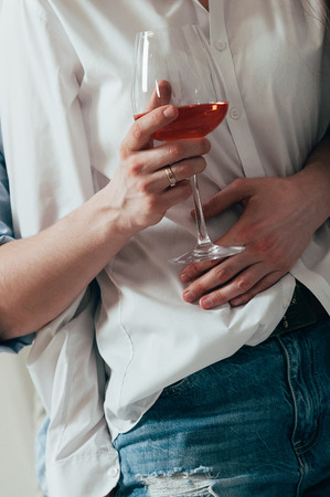 A young couple in jeans and shirts embracing and drinking wineの写真素材