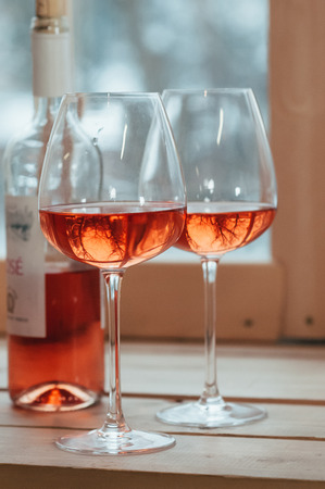 A closeup of half full bottle of rose wine and two filled glasses standing on a wooden window sillの写真素材