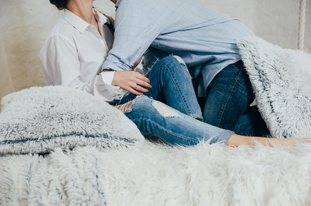 A young couple in blue jeans and white shirts having fun on a bed with pillowsの写真素材