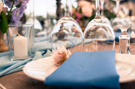 Romantic wedding or another catered event table setting, flowers, white plates, blue napkin, Easter decoration, outdoorsの写真素材