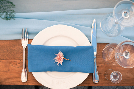 Closeup view of Wedding or other catered Event setting, flower, white plate, blue napkin, wooden table, Event decoration, outdoors, summer timeの写真素材