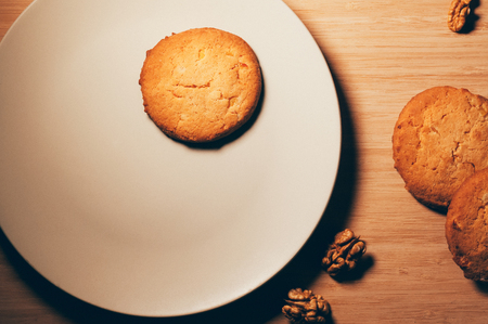 Top view of round crunchy sweet biscuits with candied fruit, wallnuts, on a white plate and wooden...
