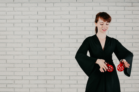 a young elegant woman in black dress, dancing flamenco with red castanets, smiling, white brick wall in the backgroundの写真素材