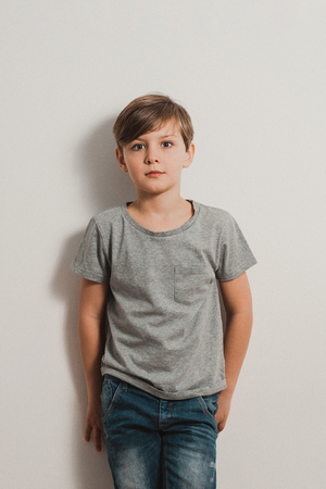 a cute boy stands next to white wall, grey t-shirt, blue jeans, frightened faceの写真素材