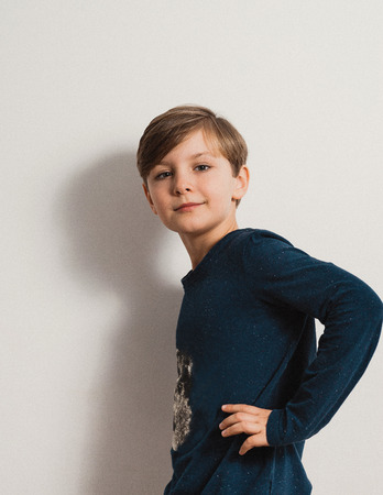 a handsome boy standing by a white wall, smiling, hand on his waist, dark blue shirtの写真素材