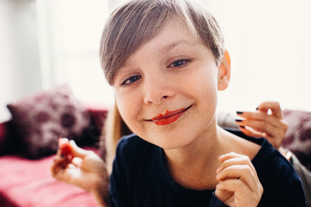 a soft focused closeup view of a cute boy with a face painted with eatable bright color cream, smiling with clown lips, a light room in the backgroundの写真素材
