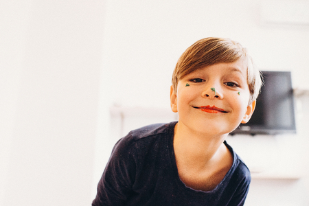 a closeup view of a cute boy with a face painted with eatable bright color cream, smiling with clown lipsの写真素材