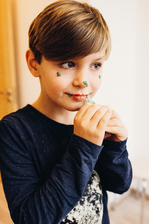 a cute boy plays painting his face with eatable bright color cream from a tube, looking like a clownの写真素材