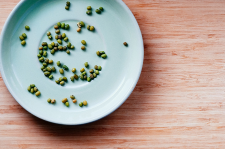 Green dry mung beans scattered on a saucer on a wooden table, top view, copy spaceの写真素材