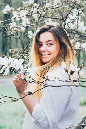 A portrait of a pretty young girl in a garden enjoying blooming trees with white flowers, cheerfully smiling, face and hair in motionの写真素材