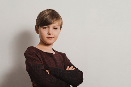 a portrait of cute boy in brown pullover, with arms crossed on breast, cold look.  White wall in the backdrop. Copy paste textの写真素材