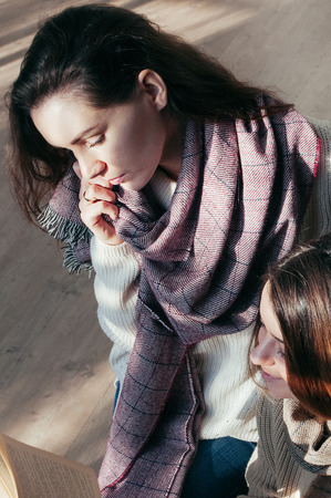 Charming young student girl friends sitting over a book, smiling, having fun. Lifestyle fashion portrait. Long hair, scarf, sweater. Natural makeupの写真素材