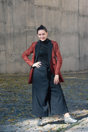 Street style Fashion portrait charming young woman in trendy clothes. Black blouse and trousers, tile red plaid jacket, silver shoes. Spring Autumn collection classic to casual lookの写真素材