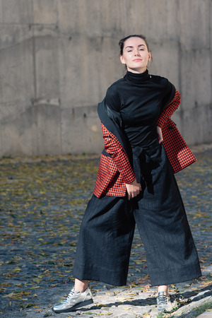Street style Fashion portrait charming young woman in trendy clothes, posing for camera. Black blouse and trousers, tile red plaid jacket, silver shoes. Spring Autumn collection classic to casual lookの写真素材