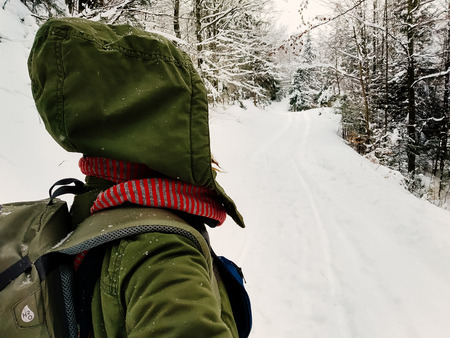 Back view young adult woman walking alone in snowy forest. Hiking and travel concept. Peaceful countryside atmosphere on a winter day. Enjoying fresh air. Close up portraitの写真素材