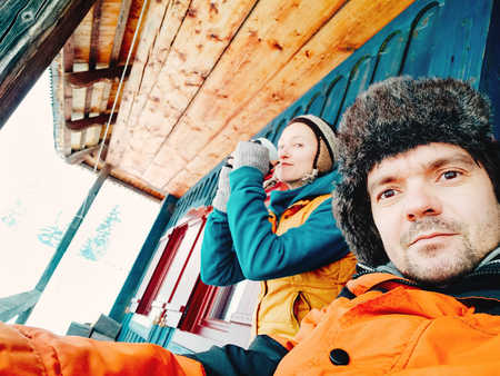 Close up portrait of young couple enjoying their drinks on a winter day. Traditional mountain village wooden house in the background. Vivid colors, blur, orange, yellowの写真素材