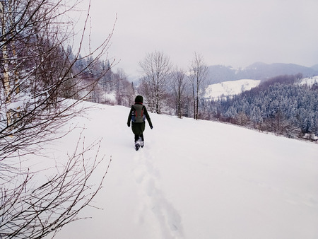 Back view Young adult woman walking alone in snowy mountains. Hiking and travel concept. Peaceful...