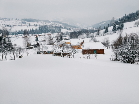 Winter countryside mountain landscape with wooden houses covered with snow, forests in the misty distant background. Picturesque and peaceful wintry scene European resort location Copy space for text の写真素材