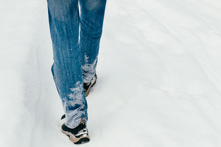 Rear view of Man walking through the deep snow on a winter day. Frozen snow on blue jeans and boots. Hiking travel extreme concept. Selective focusの写真素材