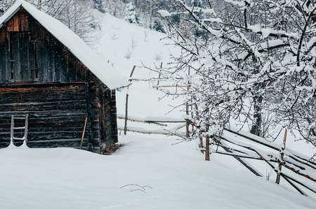 Winter countryside mountain landscape with wooden store house covered with snow, forests in the misty backdrop. Picturesque and peaceful wintry scene European resort locationの写真素材