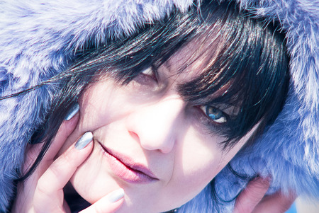 Outdoor close up portrait of young beautiful happy woman wearing purple fur hood. White skin, long dark hair, natural make up, touching face with her hand. Winter sunny day. Street fashion conceptの写真素材
