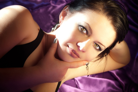 Beauty portrait of brunette woman model lying on purple silk texture as backdrop, with natural make-up. Fashion shiny highlighter on skin, sexy gloss lips. Glamour, sensual, seductive look, clean perfect skinの写真素材