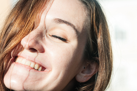 Freckled brunette young woman enjoying sunny day, natural make-up. Genuine smile, closed eyes. Pretty look, clean perfect skin. Close up view. Emotion, mimic, state of mind conceptの写真素材