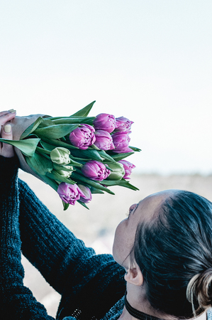 Pretty woman holding a bouquet of pink and green tulipflowers in her hands, up in the air against the sky, enjoying them, outdoors. Spring, mother day, holiday, celebration conceptの写真素材