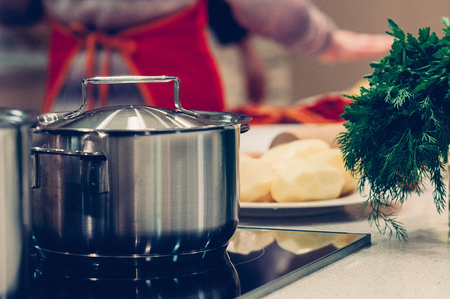 cooking pot and vegetables, healthy ingredients for soup or stew on table, woman standing in the kitchen in the background. Homemade food, cooking, vegetarian conceptの写真素材