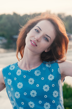 Close up portrait of young beautiful ginger haired woman, dancing, blue eyes and clothes, sunset light, summer, outdoor, motion blur, messy hair by the wind. Street fashion. Freedom conceptの写真素材