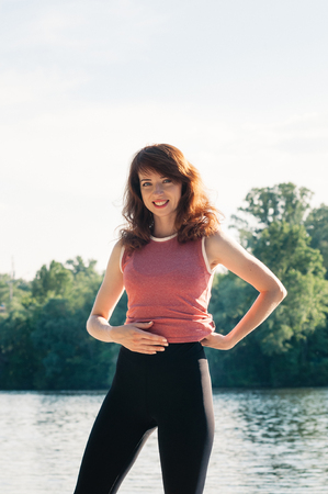 Attractive fit female practicing sports activity, yoga, wearing tight clothes, smiling, hand on her belly, long hair, water beach background. Healthy lifestyle, keep fit, weight loss conceptの写真素材