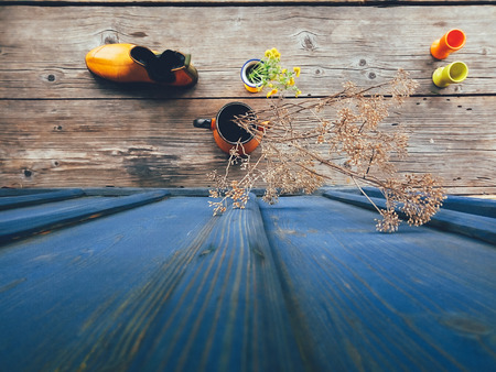 Dry flowers in orange metal jug, yellow fresh flowers, and a rubber boot, on blue wooden veranda background. Daylight. Still life in rustic style. Countryside lifestyle concept. Selective focus Top viewの写真素材