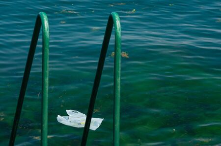 Plastic bag drifting on the sea surface, next to the beach with handhold for swimmers. Global problem of environment pollution. Ecosystem damage. Problem of marine life cleanup. Irresponsibilityの写真素材