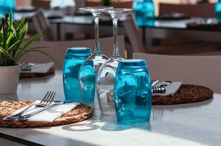 Table setup in restaurant on sunny day outdoor, served for lunch, blue glasses, wicker plates, cutlery. Simple, authentic decor. Beautiful summer holiday concept. Romantic time at resort. Selective focus の写真素材