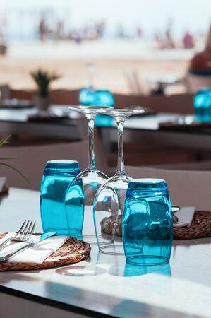 Beach cafe at day light, empty table served for lunch, glasses, wicker plates with cutlery. Simple, authentic decor. Beautiful summer holiday concept. Romantic time at resort. Selective focus の写真素材