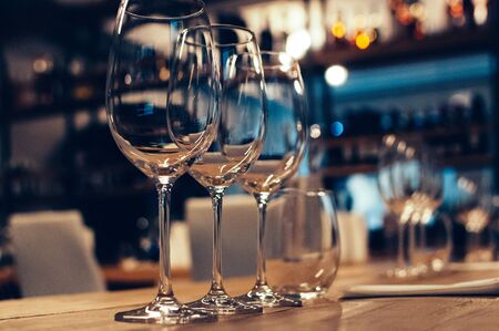 Empty glasses on wooden table, served for wine tasting event. Bar or shop interior, subdued light,...