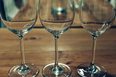 Close up image of three empty glasses with long stalks, on a wooden table, served for wine tasting event. Blurred background. Bar or restaurant interior, subdued light. Selective focus, film grain effectの写真素材
