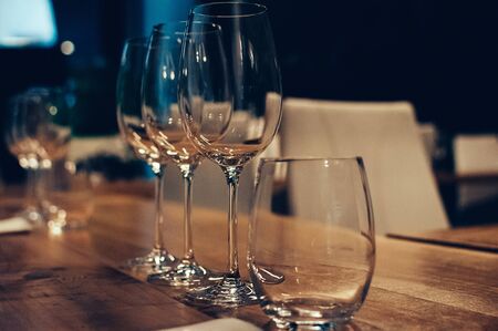 Empty glasses on wooden table, served for wine tasting event. Bar or shop interior, subdued light, lovely atmosphere. Selective focus. Film Grain effect. Low Key Imageの写真素材