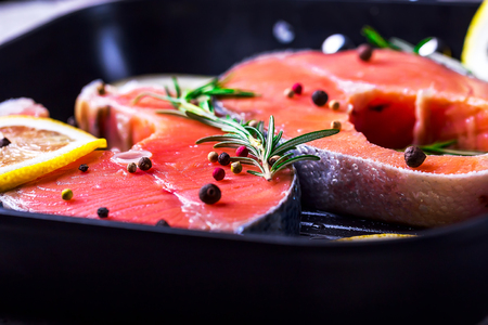 Steaks of raw salmon. Pieces of fish in a frying pan. Fish with herbs spices and lemon. Salmon is cooked for frying. Concept of a healthy dietの写真素材