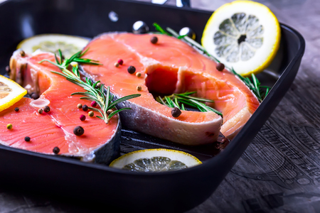 Steaks of raw salmon. Pieces of fish in a frying pan. Fish with herbs spices and lemon. Salmon is cooked for frying. Concept of a healthy dietの写真素材