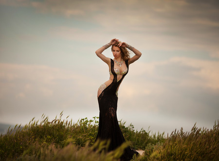 smiling young blond woman in elegant black dress running across fieldの写真素材
